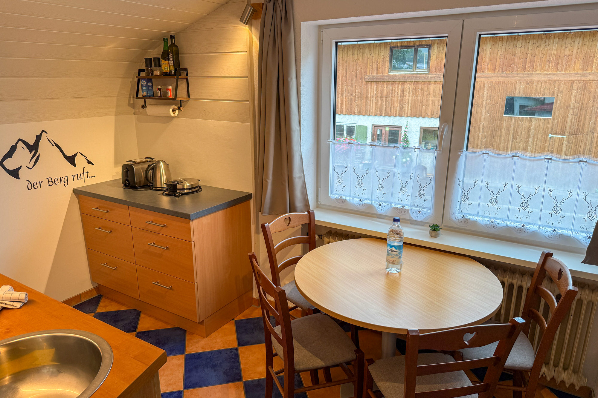 Essbereich mit Rundtisch, Fenster und Alpenmotiv auf der Gardine.