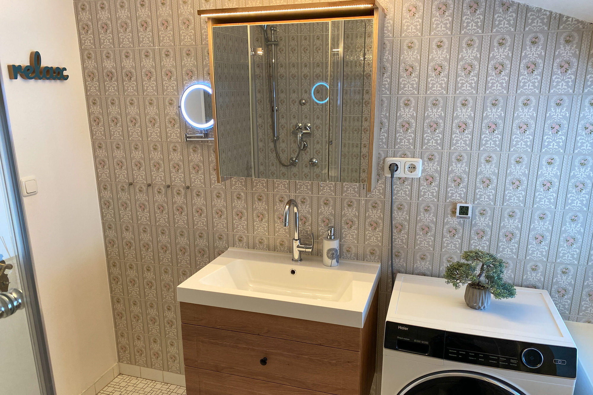 Waschtisch mit Spiegel und Dusche im Hintergrund.