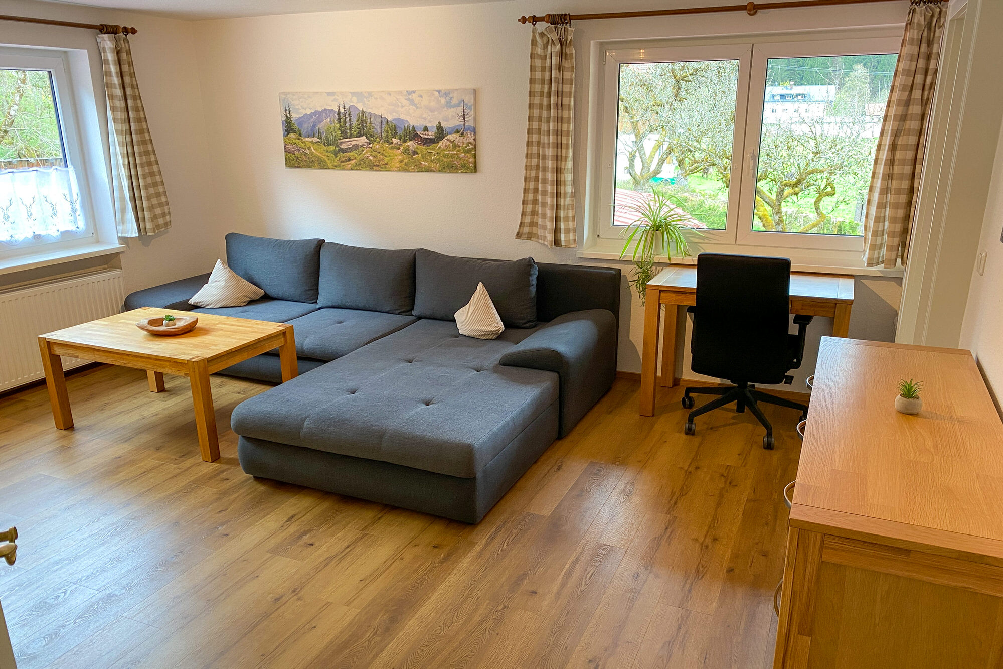 Wohnzimmer mit großer Couch, Schreibtisch und Fensterblick.
