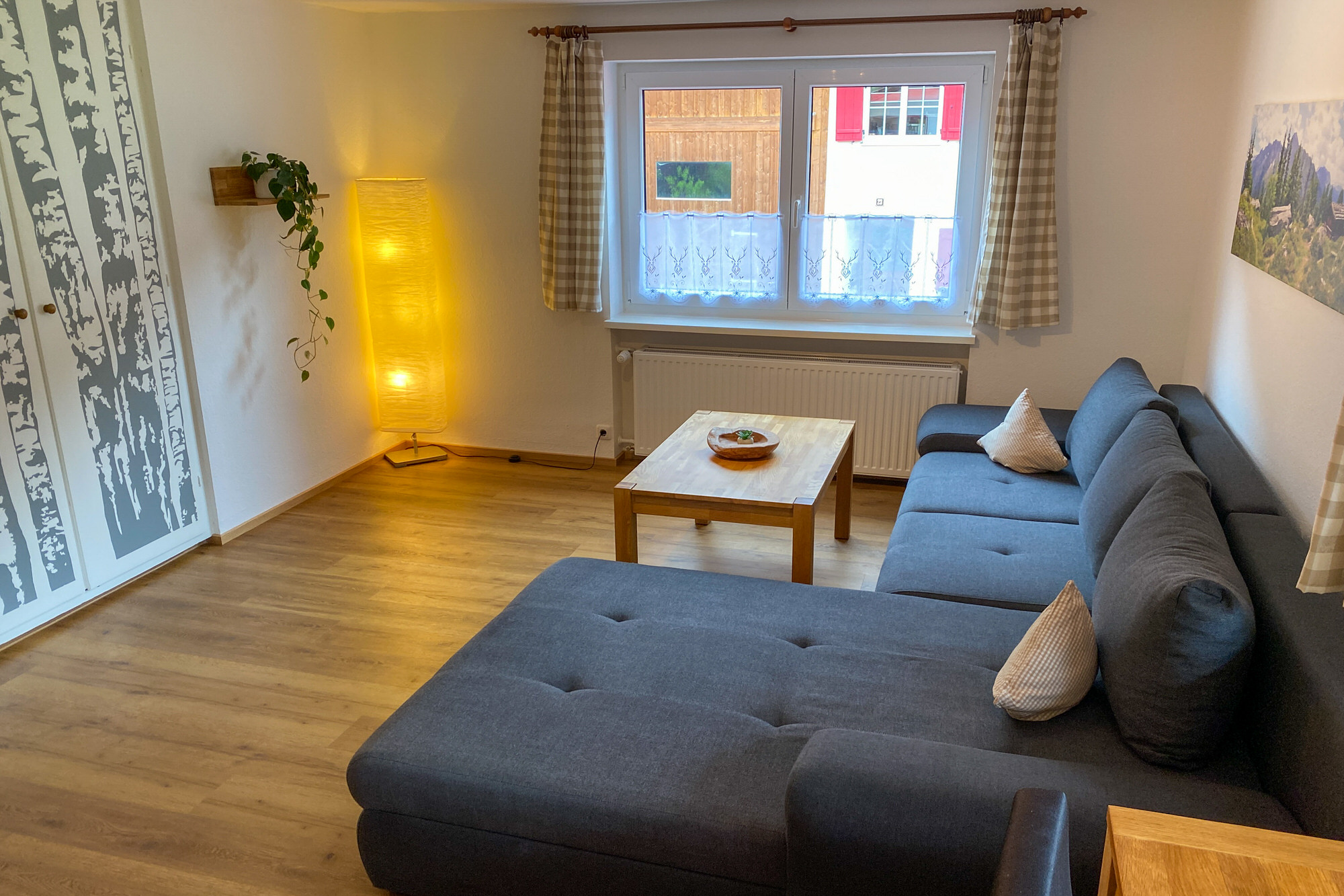 Wohnzimmer mit Couch, Vorhängen und Stehlampe im warmen Licht.