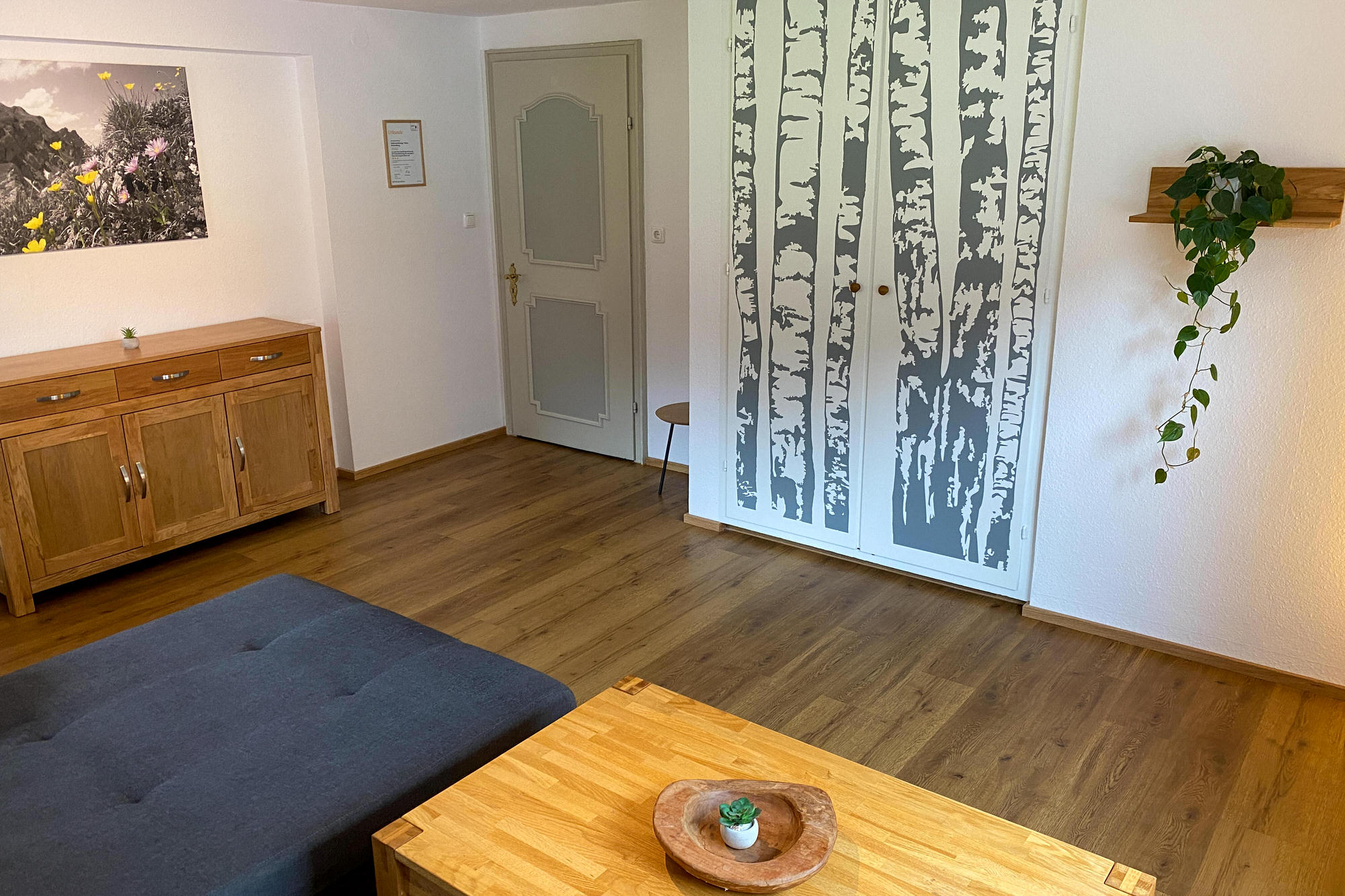 Wohnzimmer mit Couch, Kommode und stilvollem Birkenmotiv an der Wand.